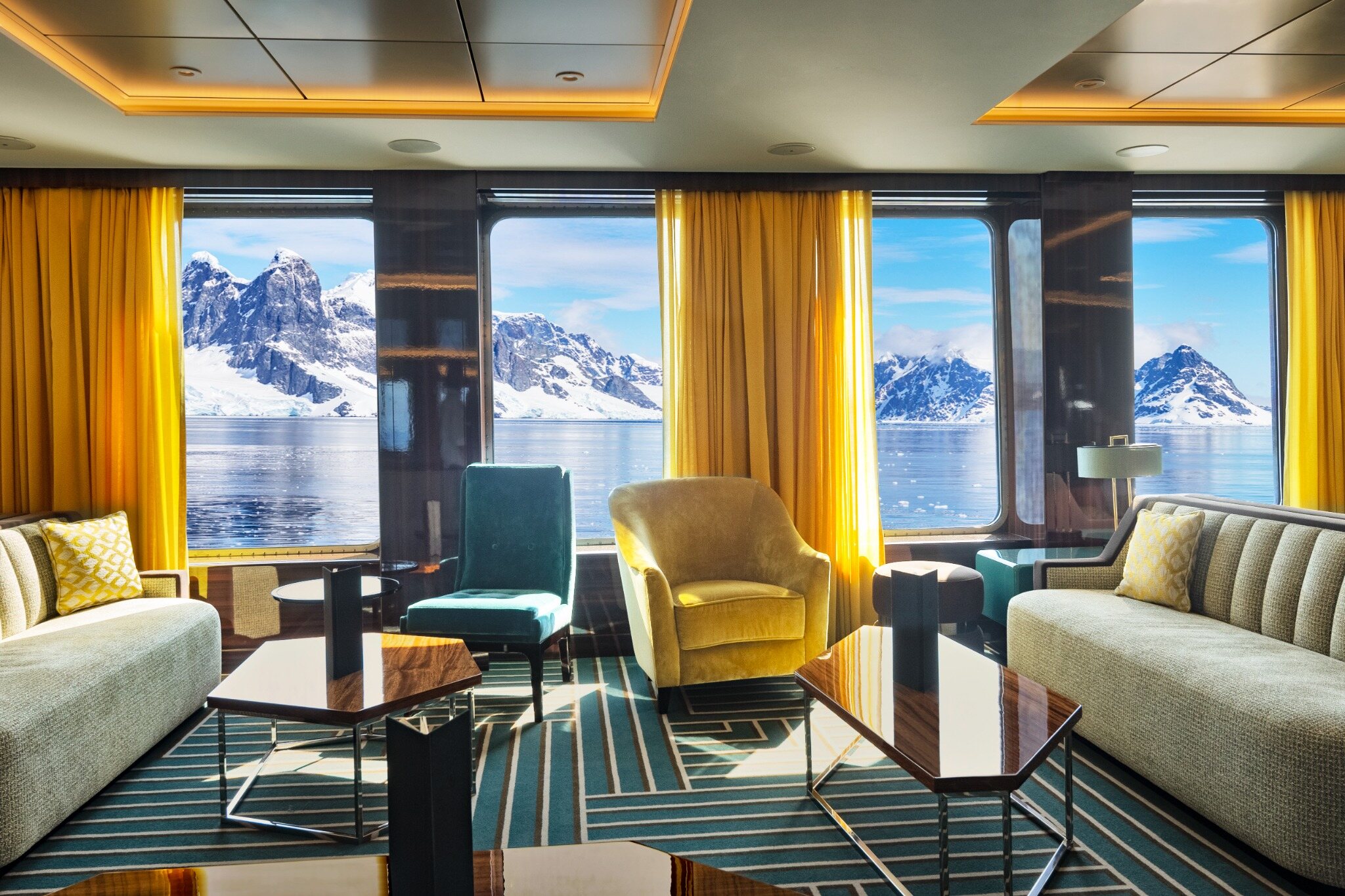 A warm, inviting expedition ship lounge with Antarctic mountains framed by the windows