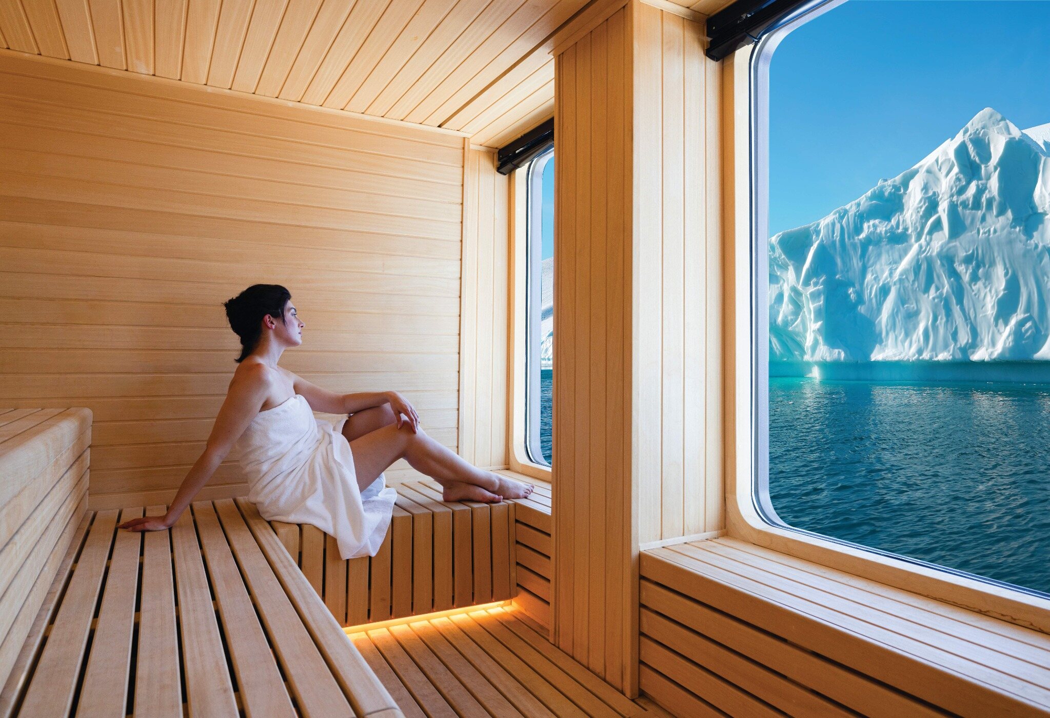 A guest relaxing in a wood-lined expedition ship sauna while an iceberg fills the view outside
