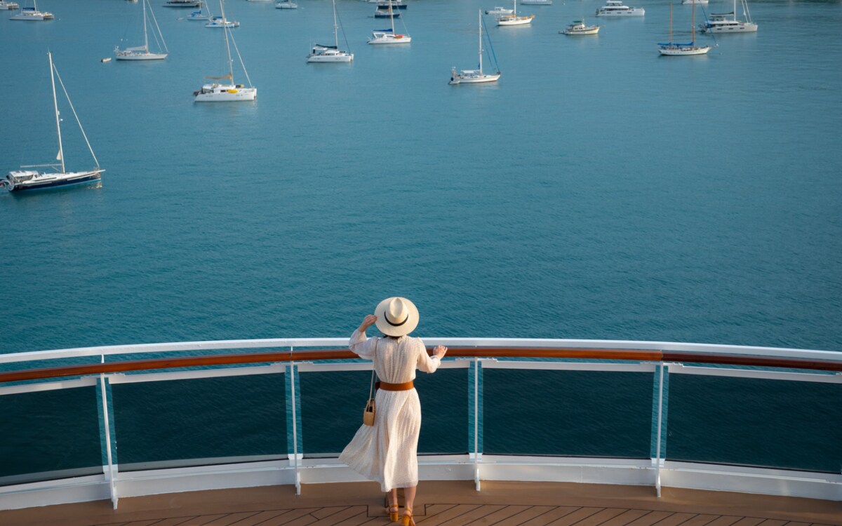 A traveler enjoying the view of sailboats from the bow of an ocean cruise ship