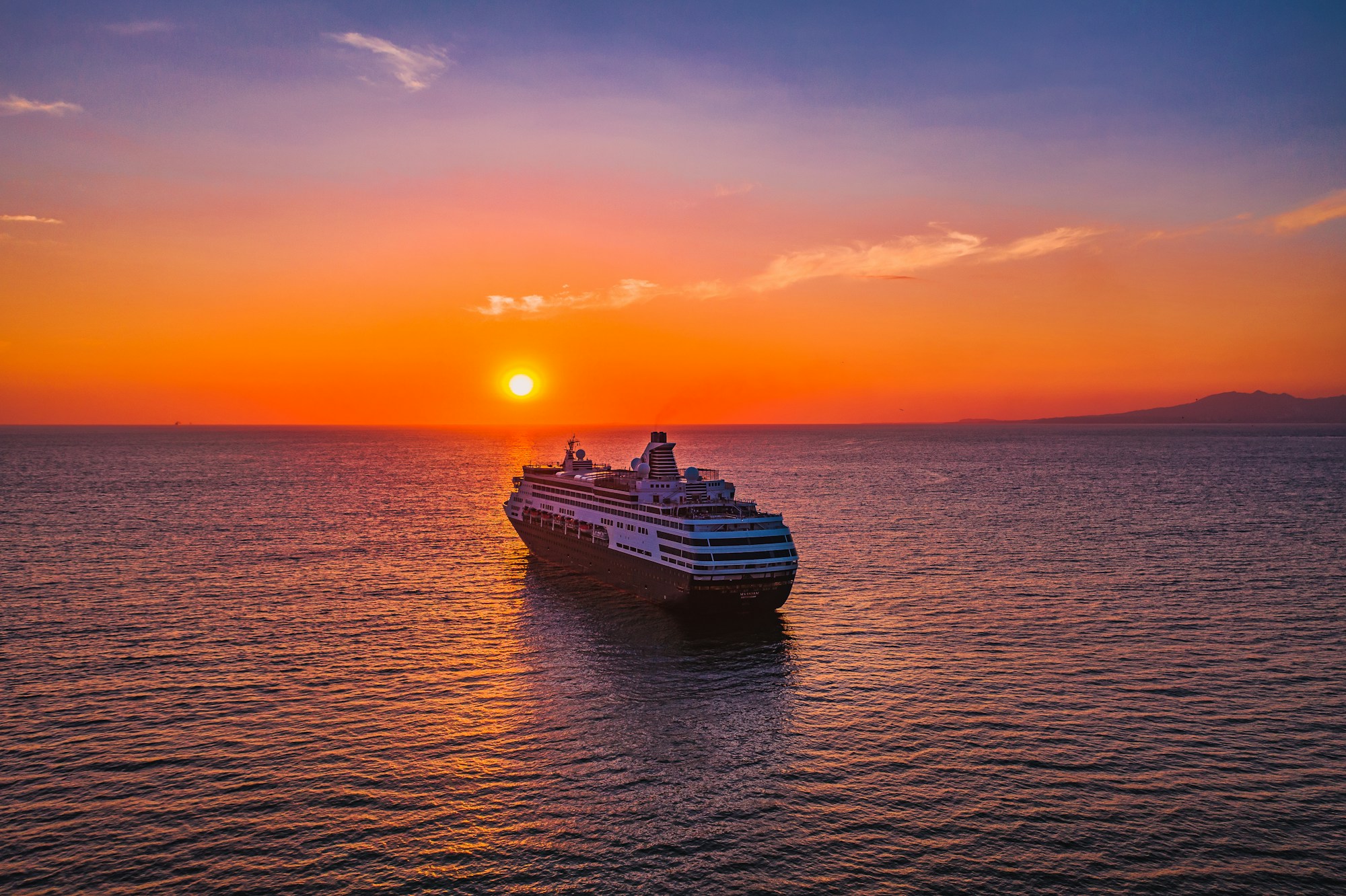 An ocean cruise ship sailing toward a vivid sunset